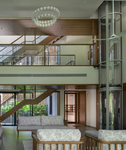 Double-height living room with glass elevator shaft, wooden staircase, orb chandelier and cane sofas