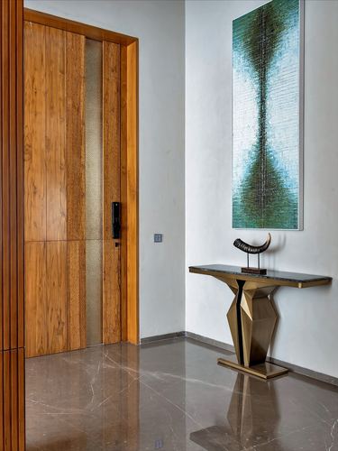 Entry foyer with wooden panelled door, geometric brass console table, and vertical art panel