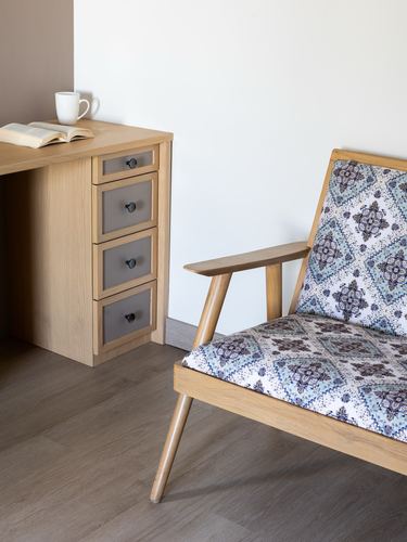 Wooden desk with drawers beside a mid-century armchair with patterned cushion