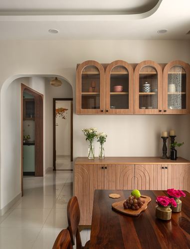 Dining room with arched wood-and-glass cabinets above a fluted sideboard, seen through an arched hallway opening