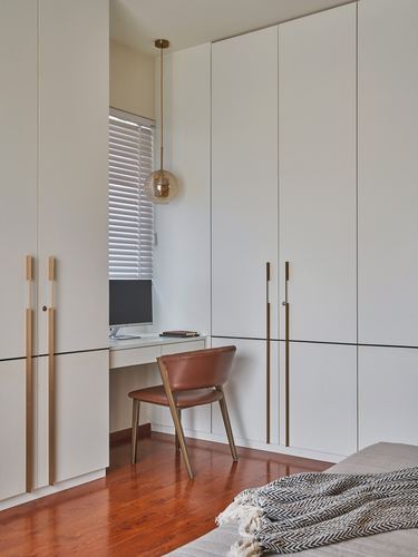 Built-in wardrobe wall with recessed study nook, leather chair and pendant light over desk