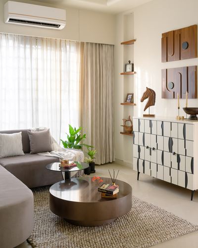 Living room with grey sectional sofa, round drum coffee table, and patterned wood sideboard beneath wall art