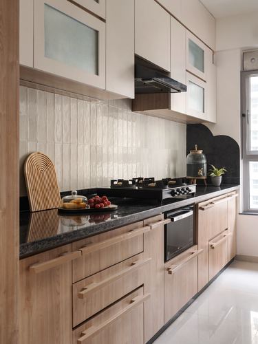 Galley kitchen with wood cabinetry, ribbed cream tile backsplash and black stone counter