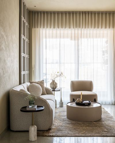 Curved beige boucle sofa and armchair around a round coffee table by sheer curtained windows