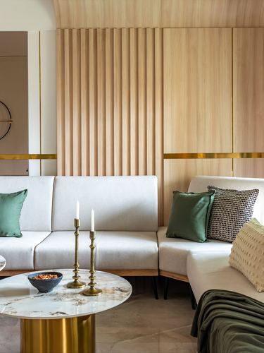 Living room corner with fluted wood wall, brass candlesticks, and green cushions on a beige sofa