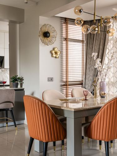 Dining table with orange channel-tufted chairs beneath a gold globe chandelier and floral wall sconces