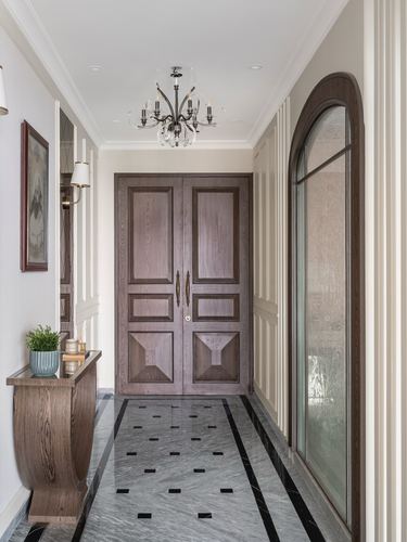 Marble-floored entry hallway leading to a panelled wooden double door beneath a chandelier