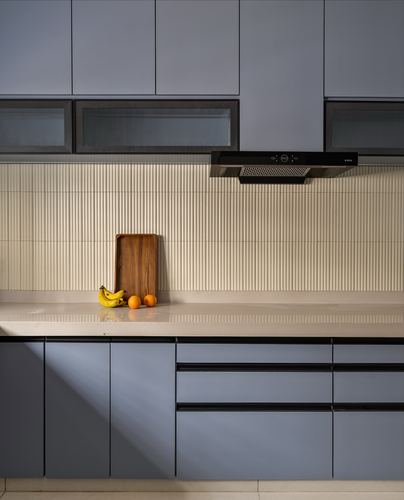 Blue kitchen cabinetry with fluted cream backsplash, black chimney hood, and fruit on counter
