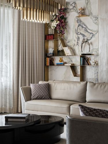 Living room corner with marble wall, brass shelving unit, chandelier, and cream leather sofa