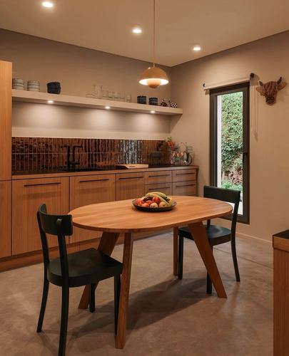 Wood-toned kitchen-dining nook with oval table, black chairs, and glass door opening to greenery