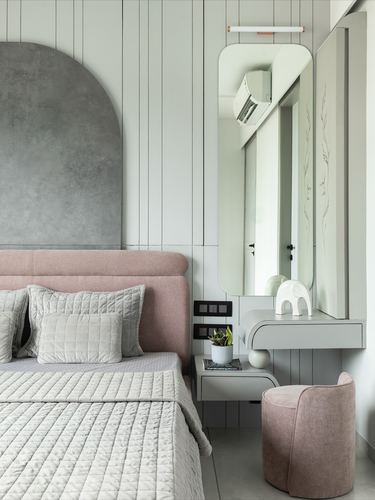 Pastel pink bedroom corner with upholstered headboard, arched mirror, and small built-in vanity nook