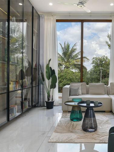 Living room corner with sectional sofa, glass shelving, and floor-to-ceiling window overlooking palm trees