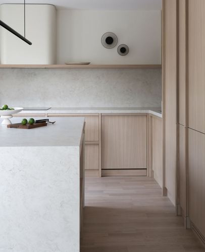 Minimalist kitchen with waterfall stone island, light wood cabinetry, and wall-mounted ceramic discs