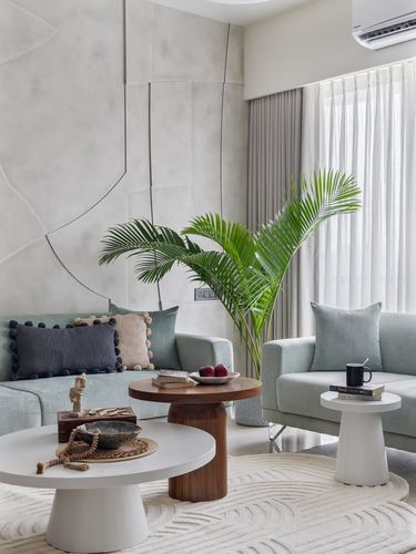 Sage green sofas around round wood-and-white coffee tables beneath a textured sculptural wall panel