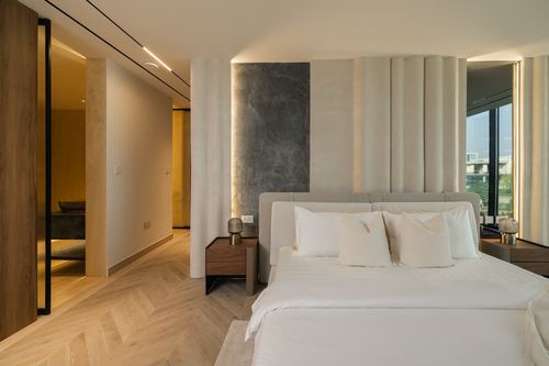 Bedroom with ribbed upholstered headboard wall, stone accent panel, chevron wood floor and walk-in view beyond