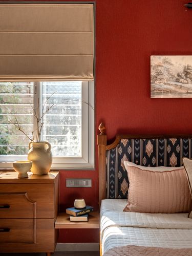 Bedroom corner with red wall, wooden dresser, patterned headboard, and window light