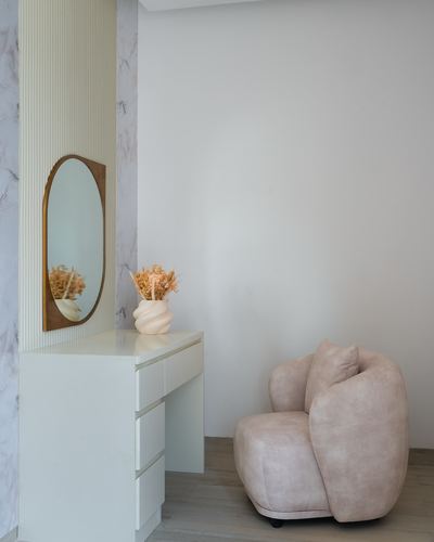 White console with oval mirror and dried flowers beside a curved blush armchair