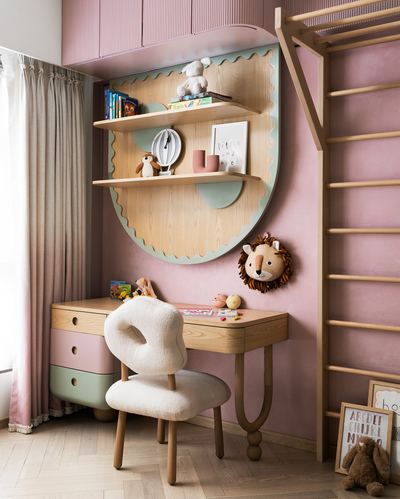 Child's study nook with scalloped wooden shelf, pink cabinetry, boucle chair, and wall ladder
