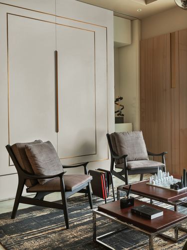 Two dark wood armchairs face brass-inlaid coffee tables against a paneled wall with brass inlay detail