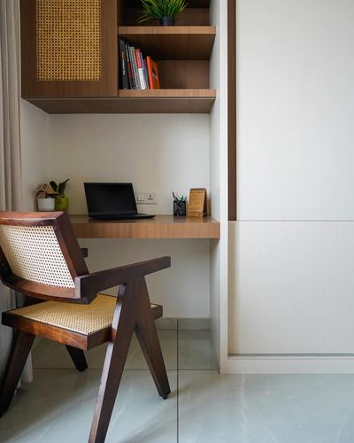 Compact study nook with cane chair, floating wood desk and laptop under open wood shelving