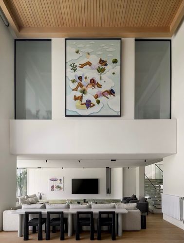 Double-height living room with large painting above a mezzanine, dining table and sofas below
