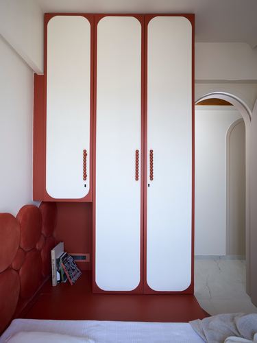 Terracotta red wardrobe with white curved doors beside an arched doorway in a bedroom