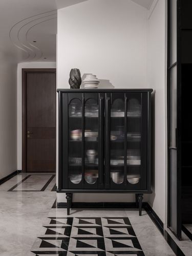 Black cabinet with reeded glass doors in a marble-floored corridor with geometric inlay