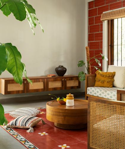 Kerala-style living room with cane sofa, round wooden table, and red exposed brick niche