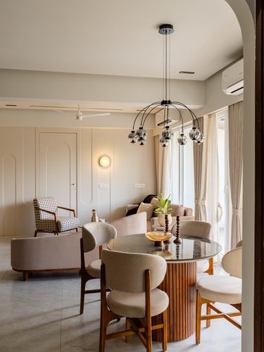 Dining area with round marble table, fluted wood base, and cluster pendant light seen through an arch