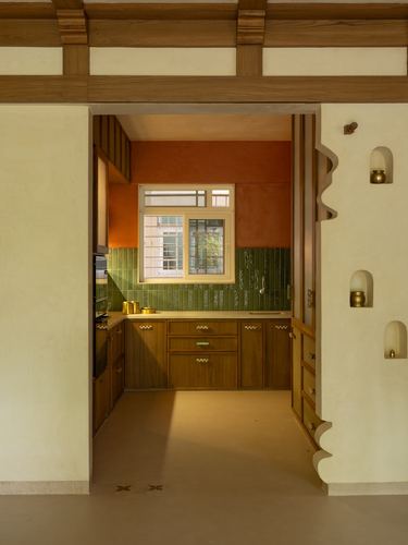 View through a carved wooden doorway into a kitchen with terracotta walls and green tile backsplash