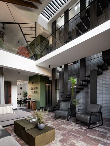 Double-height living room with black steel staircase, tiled walls, and stone floor