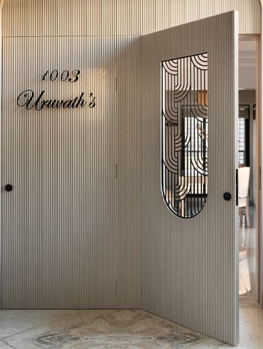 Fluted entrance door with art deco grille window opening into a Mumbai apartment foyer