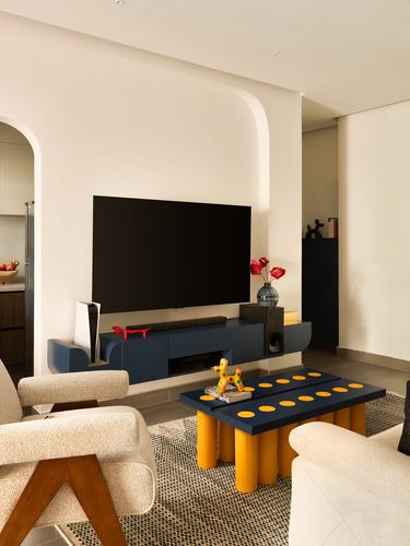 Living room with navy TV console, mustard-legged coffee table, boucle armchairs and arched niche