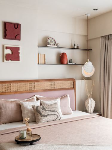 Bedroom with cane headboard, pink linens, floating shelves and a textured pendant light