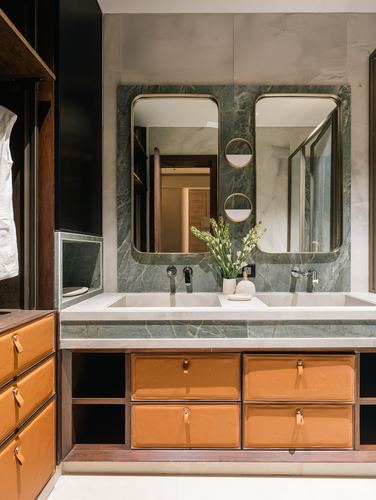 Double vanity with green marble wall, brass mirrors and tan leather drawers in Ahmedabad home
