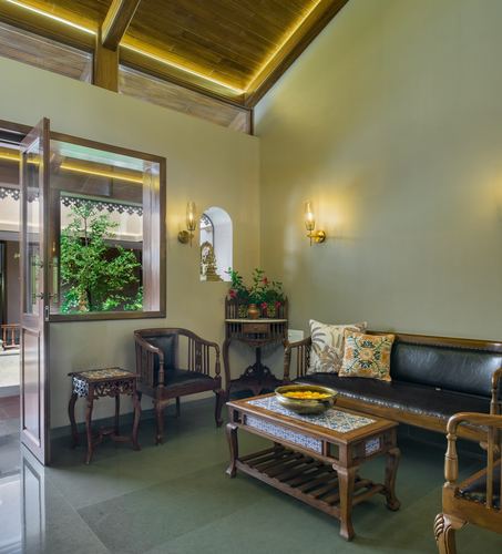 Traditional wada-style living room with teak furniture, carved bench, and arched deity niche under sloped wooden ceiling