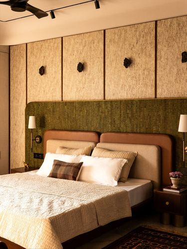 Bedroom with olive and tan leather headboard beneath textured panelled wall and dark sconces