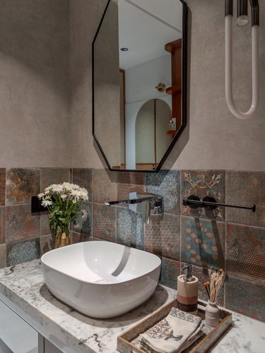 Vessel sink on stone counter beneath octagonal mirror and patterned tile backsplash in bathroom