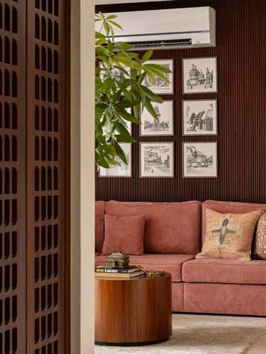 View through a carved wooden jali door into a living room with a terracotta sofa and gallery wall.