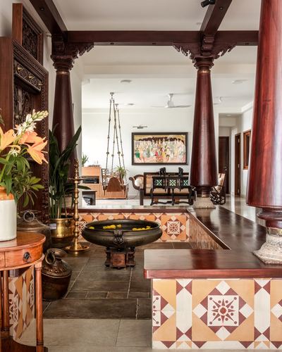 Chettinad-style foyer with carved wooden pillars, hanging swing, brass urli and patterned tile border