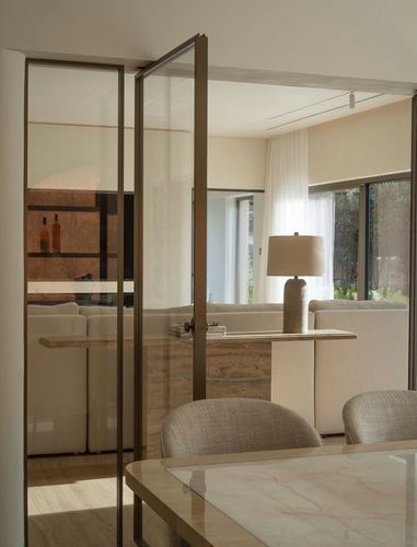 Bronze-framed glass pivot doors open onto a living room with a marble console and sheer curtains