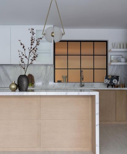 Minimalist kitchen island in white oak with marble counter, backlit amber fluted glass window behind