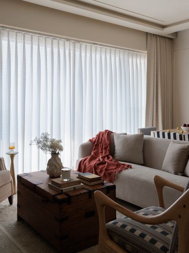 Living room with beige sofa, coral throw, wooden trunk table and sheer curtained window