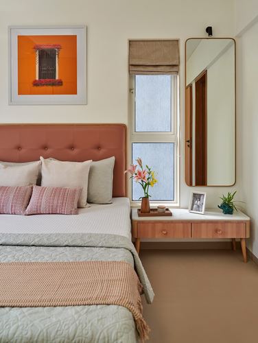 Bedroom with terracotta tufted headboard, framed orange window art, and a floating wood console under a tall mirror