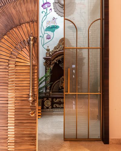 Fluted wood archway and bronze glass door frame a carved wooden mandir beyond