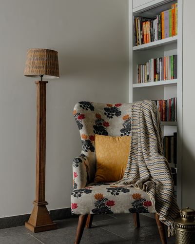 Floral wingback armchair with mustard cushion beside wooden floor lamp and bookshelf