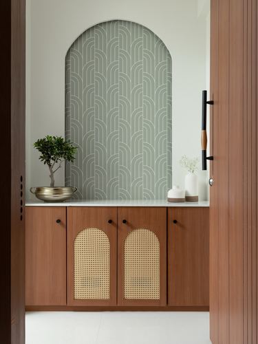 Arched patterned niche above wooden console with cane-front cabinets and bonsai plant