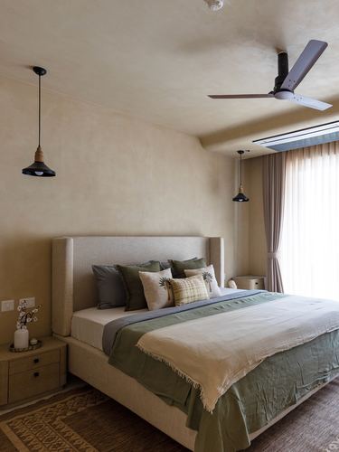Neutral-toned bedroom with upholstered headboard, green and cream bedding, and two black pendant lights.