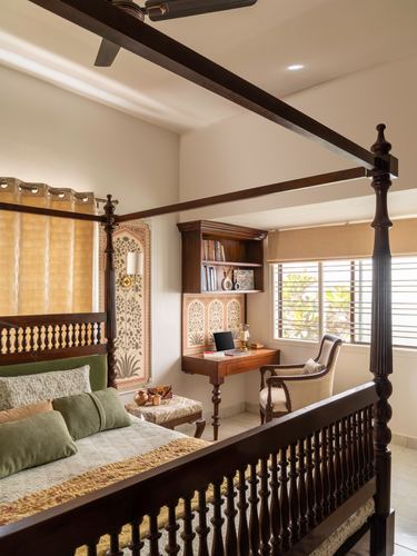 Traditional carved wood four-poster bed beside a built-in study nook with arched decorative panel