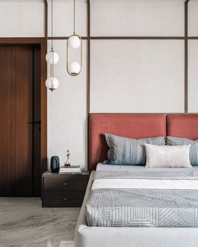 Bedroom with coral velvet headboard, brass pendant lights, marble floor and wood door